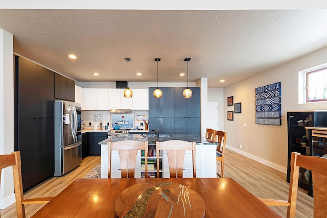 kitchen with a breakfast bar area, a kitchen island with sink, light wood finished floors, smart refrigerator, and pendant lighting