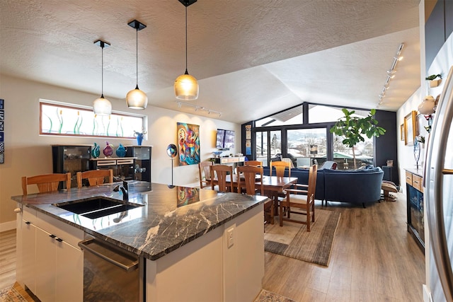 kitchen featuring decorative light fixtures, open floor plan, a kitchen island with sink, a sink, and white cabinetry