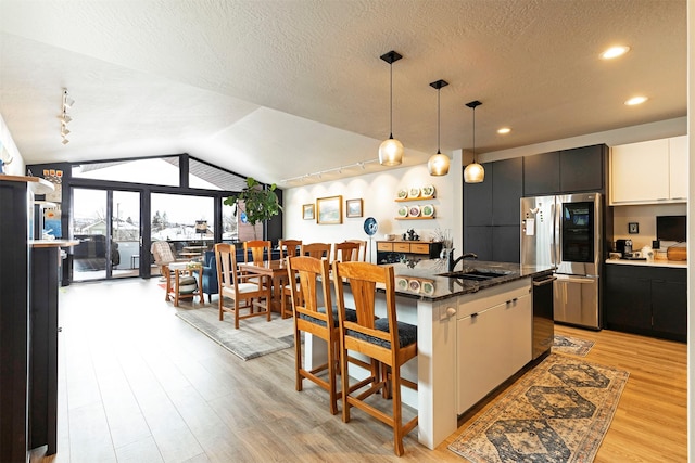 kitchen with hanging light fixtures, a kitchen island with sink, vaulted ceiling, stainless steel appliances, and white cabinetry