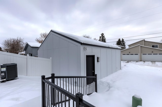 snow covered structure with an outdoor structure, fence, and central AC unit