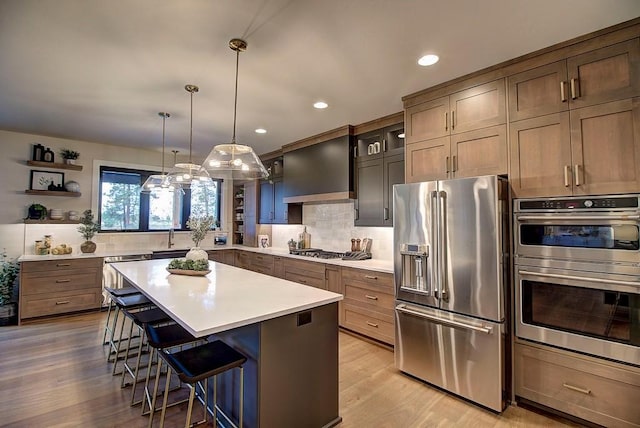 kitchen featuring appliances with stainless steel finishes, a breakfast bar area, a center island, light countertops, and wall chimney range hood