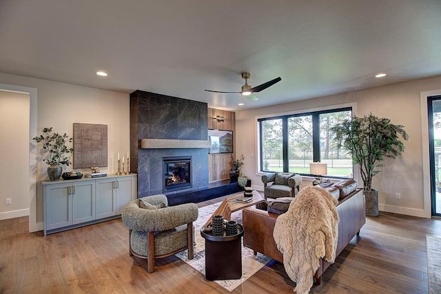 living room featuring baseboards, light wood finished floors, a high end fireplace, and recessed lighting