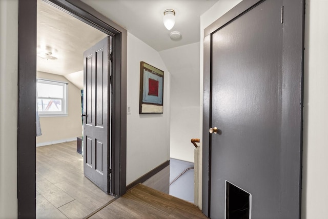 hall featuring light wood-style floors, lofted ceiling, and baseboards