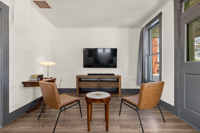 living area with ornamental molding, dark wood finished floors, visible vents, and baseboards