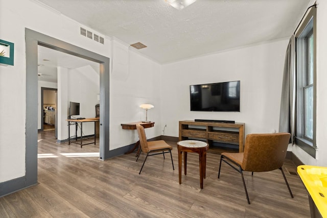 sitting room with visible vents, a healthy amount of sunlight, a textured ceiling, wood finished floors, and baseboards