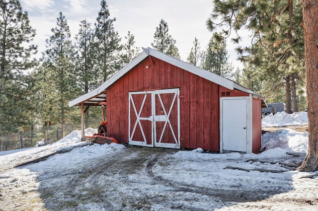 snow covered structure with an outdoor structure, a barn, and fence