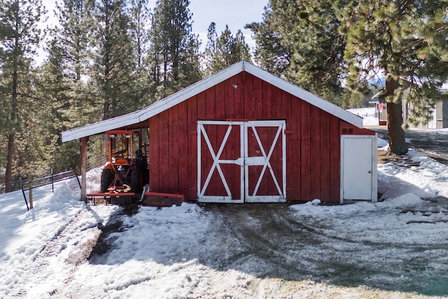 snow covered structure with a barn, fence, and an outbuilding