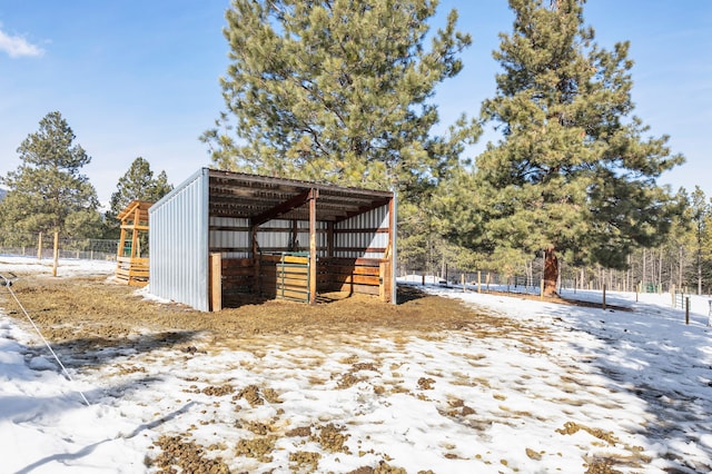 snow covered structure featuring a carport and an outbuilding