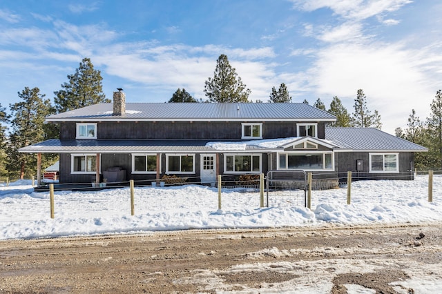 snow covered property featuring metal roof and a chimney