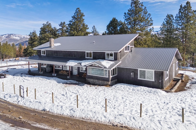 snow covered property with metal roof, a mountain view, and a chimney