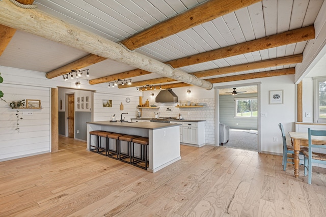 kitchen featuring white cabinets, light wood-style flooring, a breakfast bar area, rail lighting, and beam ceiling