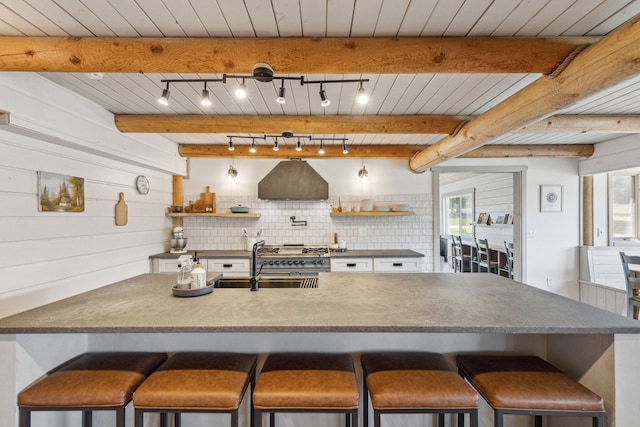 kitchen featuring beamed ceiling, ventilation hood, a breakfast bar area, and a sink