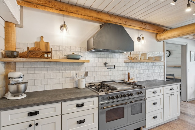 kitchen featuring range with two ovens, white cabinets, wall chimney range hood, and open shelves