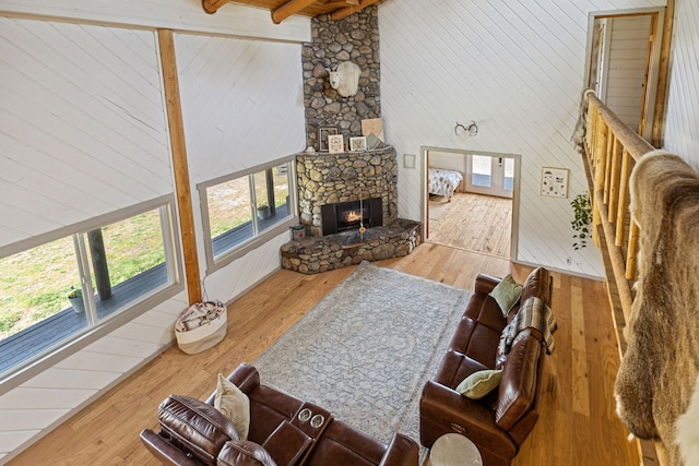 living room featuring a stone fireplace, hardwood / wood-style flooring, wooden walls, a high ceiling, and beamed ceiling