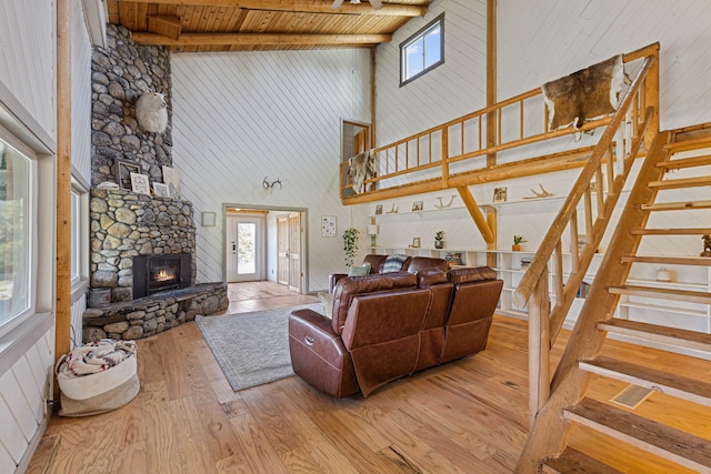 living area featuring stairs, a healthy amount of sunlight, a stone fireplace, and hardwood / wood-style flooring