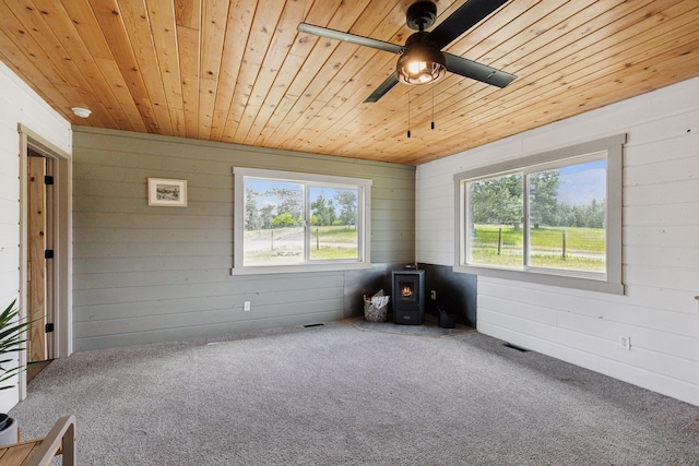 unfurnished room with carpet floors, wood ceiling, a wood stove, ceiling fan, and wooden walls