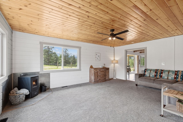 living area with a ceiling fan, wood ceiling, a wood stove, and light carpet