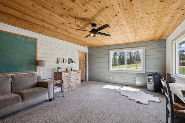 living room featuring a ceiling fan, wooden ceiling, carpet flooring, and a wood stove