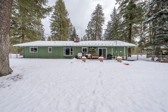 snow covered rear of property with board and batten siding, fence, and a chimney