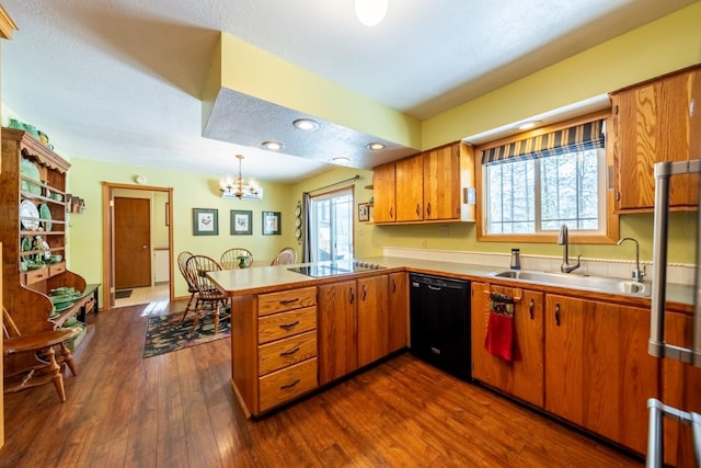 kitchen with brown cabinetry, decorative light fixtures, a peninsula, black appliances, and a sink