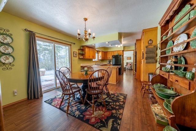 dining area with a textured ceiling, dark wood-type flooring, baseboards, and an inviting chandelier