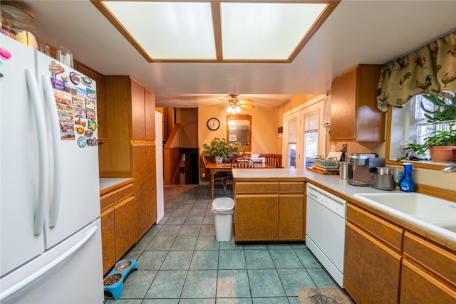 kitchen featuring light tile patterned floors, a peninsula, white appliances, light countertops, and brown cabinets