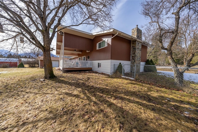 view of property exterior featuring a chimney, fence, a deck, and a yard