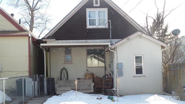 snow covered house featuring fence and stucco siding