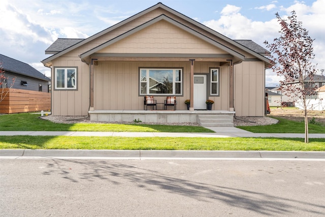 bungalow featuring covered porch, fence, a front lawn, and board and batten siding