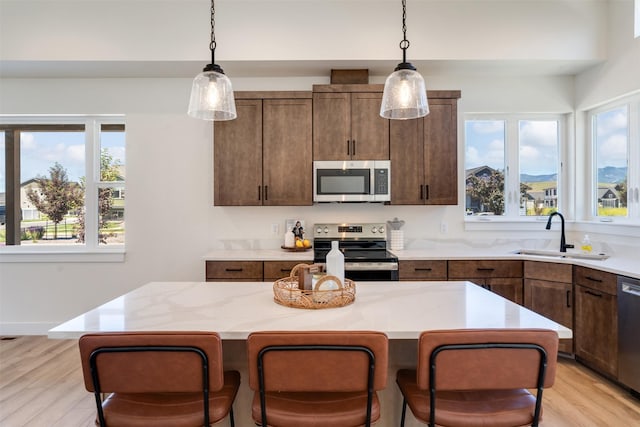 kitchen with light stone counters, a center island, pendant lighting, stainless steel appliances, and a sink