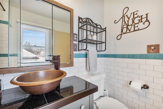 bathroom with toilet, tile walls, a sink, and wainscoting