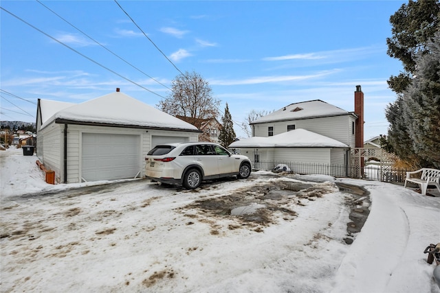 snow covered garage featuring fence and a detached garage