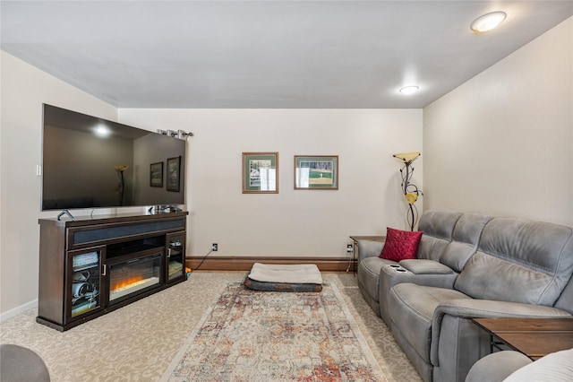 living area featuring carpet, a glass covered fireplace, and baseboards