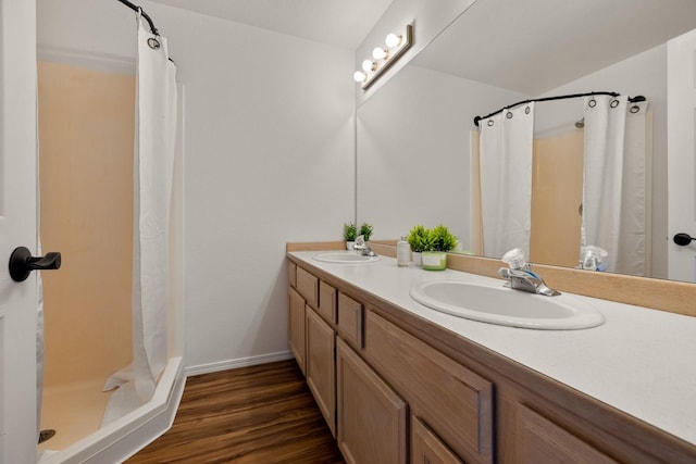 full bath featuring double vanity, a sink, a shower stall, and wood finished floors