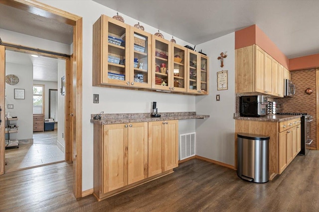 kitchen featuring visible vents, dark countertops, glass insert cabinets, stainless steel appliances, and light brown cabinets