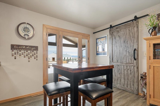 dining room featuring a barn door, baseboards, and wood finished floors