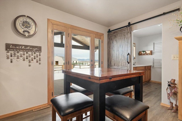 dining room featuring a barn door, visible vents, light wood-style flooring, and baseboards