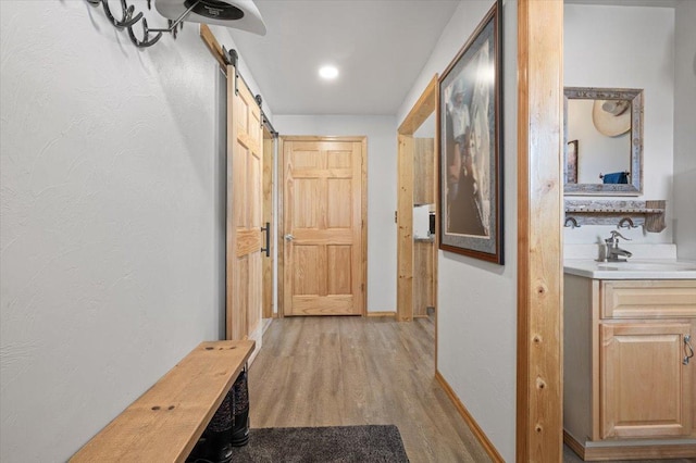 corridor featuring a barn door, baseboards, a textured wall, light wood-type flooring, and a sink