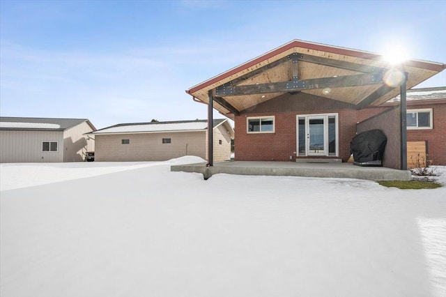 snow covered rear of property with french doors and brick siding