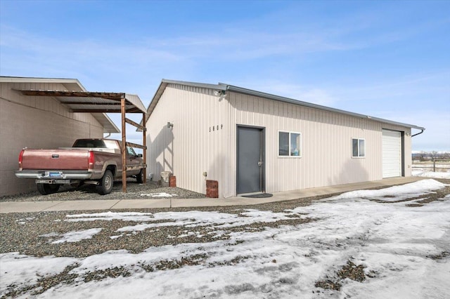 snow covered rear of property featuring a carport and a detached garage