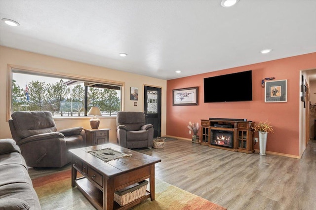 living area with recessed lighting, baseboards, wood finished floors, and a glass covered fireplace