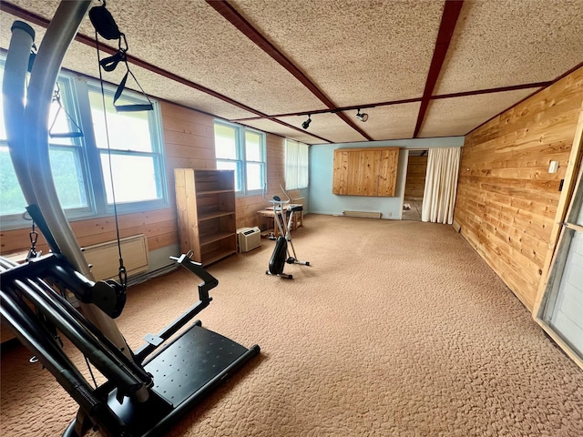 exercise room featuring carpet floors, wooden walls, and a textured ceiling