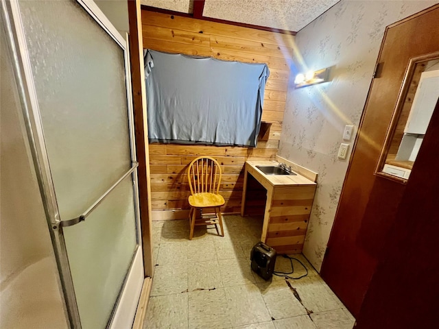 bathroom with wallpapered walls, an enclosed shower, a sink, wooden walls, and tile patterned floors