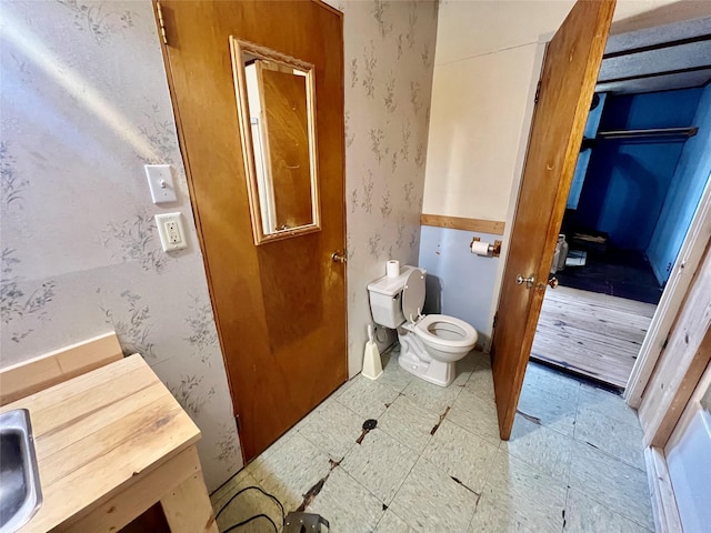 bathroom with a sink, toilet, and wallpapered walls