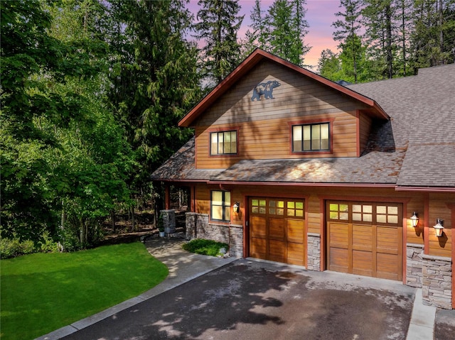 chalet / cabin featuring aphalt driveway, a front yard, stone siding, and a garage