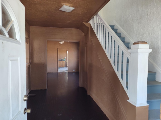 hallway with a textured wall, stairway, and dark wood-style flooring