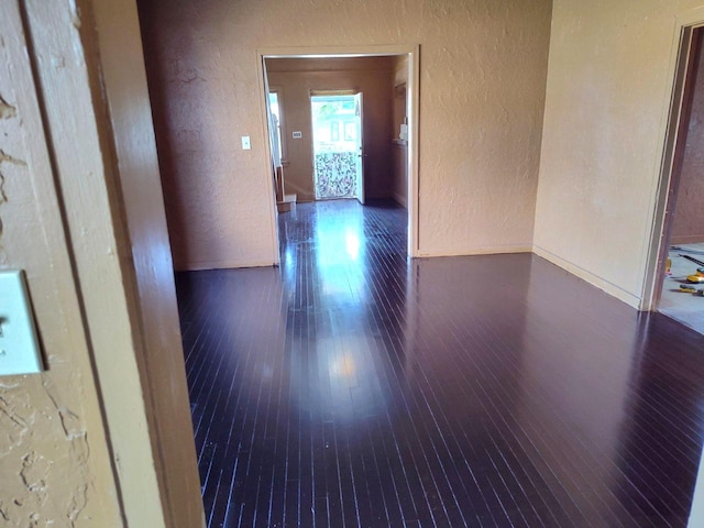 hallway with a textured wall, dark wood finished floors, and baseboards