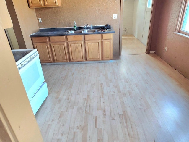 kitchen featuring white electric range oven, a textured wall, dark countertops, brown cabinets, and a sink