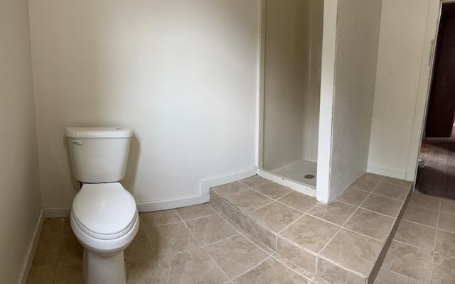 full bathroom featuring a stall shower, baseboards, toilet, and tile patterned floors