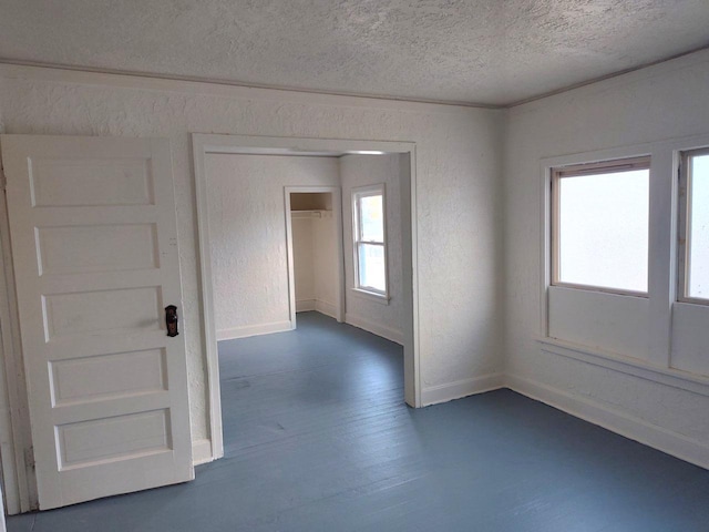 empty room with plenty of natural light, dark wood-style flooring, and a textured wall